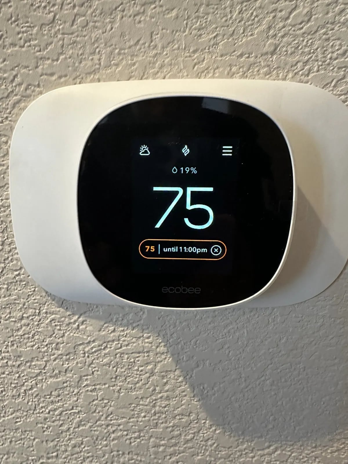 An ecobee thermostat set to 75 degrees on a textured wall