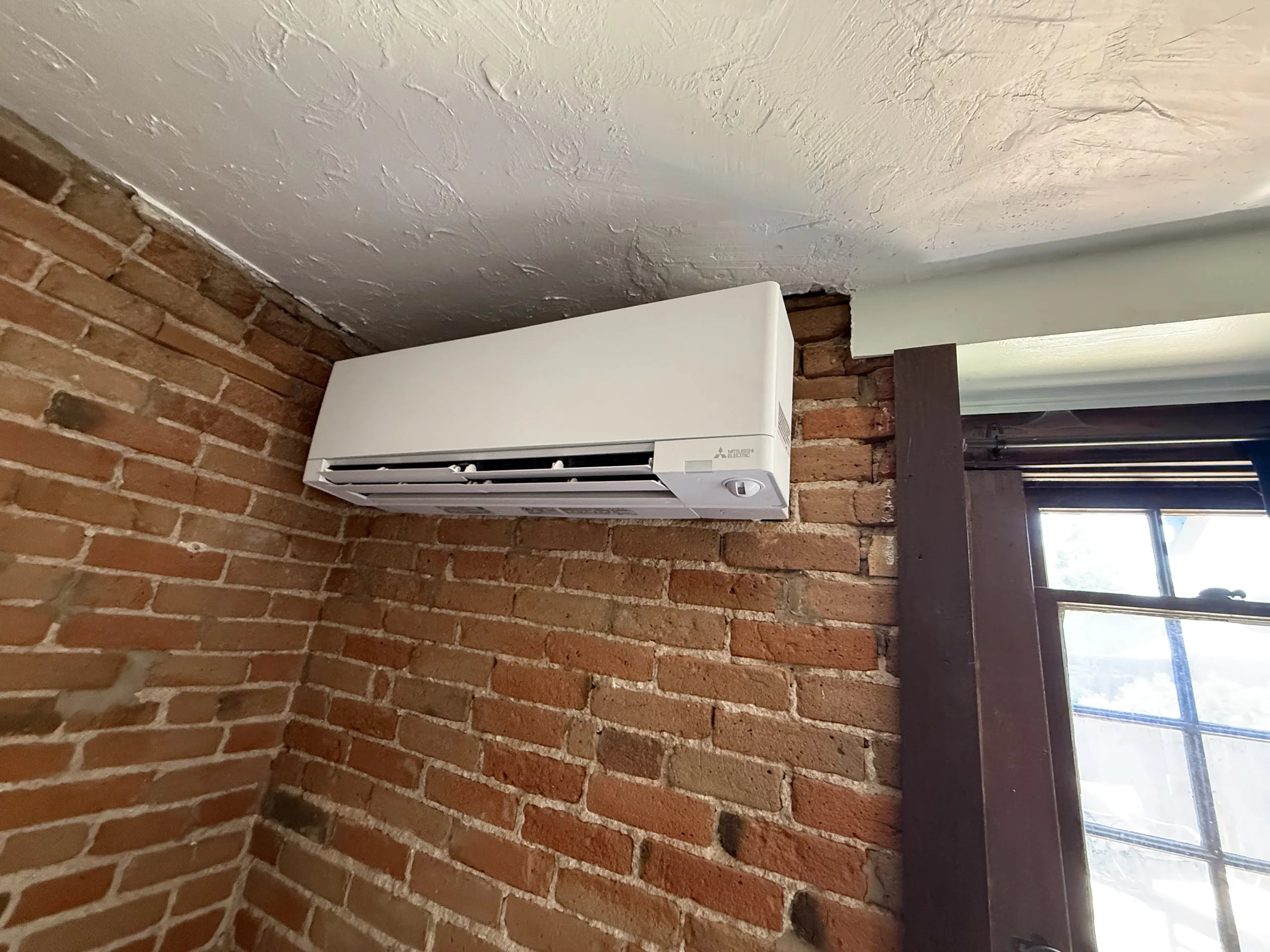 A Mitsubishi wall-mounted head in the corner of a red brick room